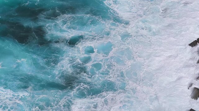 Top-down view of powerful Atlantic waves swirling over rocks near Mesa del Mar, Tenerife, Spain. Turquoise ocean water and white foam patterns creating abstract sea motion