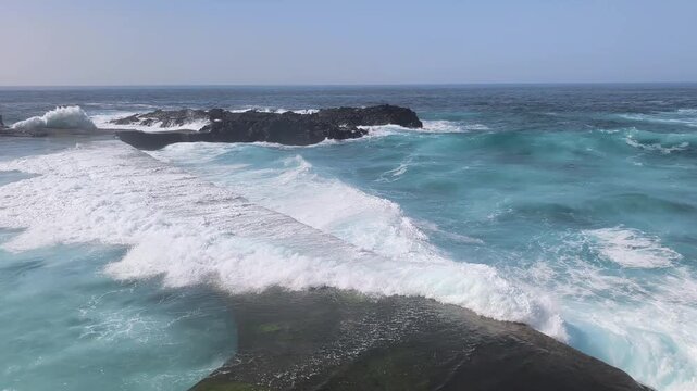 Atlantic waves washing over coastal breakwater and natural sea pool in Mesa del Mar, Tenerife, Spain. Turquoise ocean water and volcanic coast. Concept of coastal erosion and powerful sea