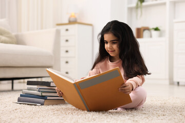 Fototapeta premium Cute little girl reading book on floor at home