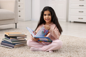Fototapeta premium Cute little girl reading book on floor at home