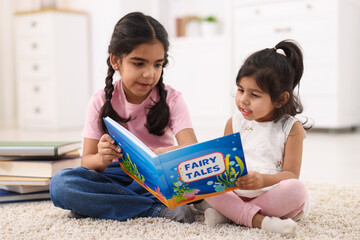 Fototapeta premium Cute little girls reading book together at home