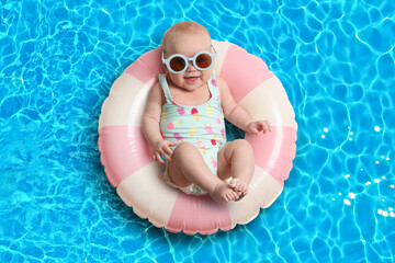Cute little baby with sunglasses on inflatable ring in swimming pool, above view