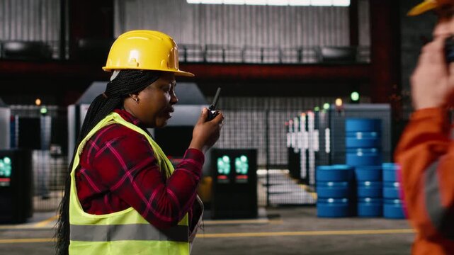 Woman engineer, portable walkie-talkie, speak with colleagues, walking across warehouse, worker supervising machinery hall workstations. Wireless radio transceiver near sparks from welding.