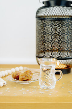 One fluted glass of armudu with water, dates and a lantern on the table.