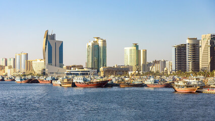 Obraz premium Modern skyline of Dubai Creek with traditional cargo dhow boats at the pier
