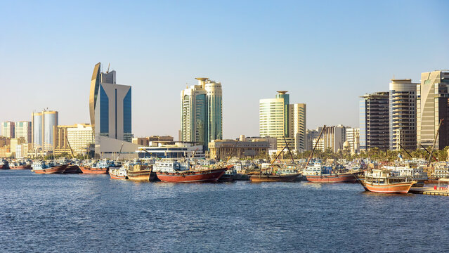 Modern skyline of Dubai Creek with traditional cargo dhow boats at the pier