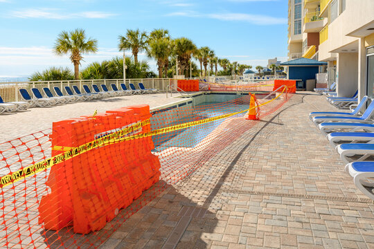 An emptied out, closed for service resort swimming pool  under maintenance surrounded by safety barriers and mesh along the Grand Strand Atlantic Ocean at Myrtle Beach, South Carolina.