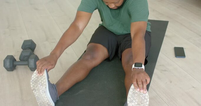 African American man following phone cue, stretching hamstring on black mat and reaching shoes