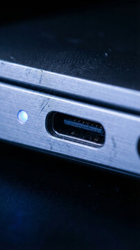A macro close-up of a USB-C port on a metallic chassis with a soft blue LED indicator light glowing in the dark.