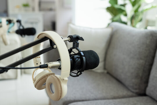 Black microphone with foam windscreen is sitting on boom, tan headphones are hanging in home studio