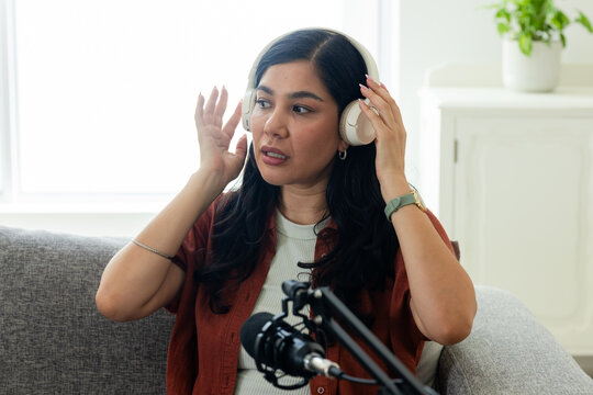 Mid-30s woman adjusting over-ear headphones while preparing to speak into microphone at home studio