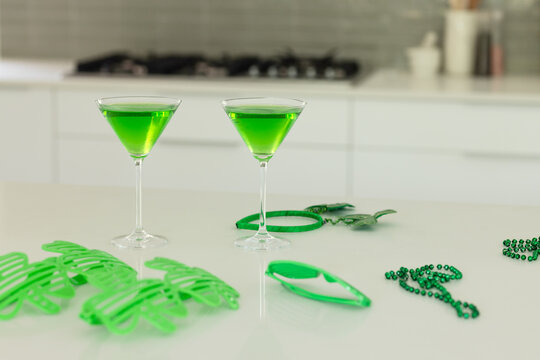 Two martini glasses are resting on kitchen counter with neon green cocktails, sunglasses, beads