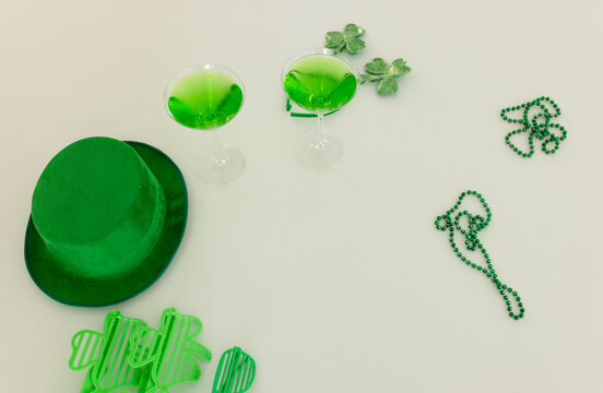 Green hat sitting left, coupes holding green drinks, shamrock beads scattering on table, copy space