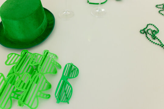 Green top hat, shutter shades, beads, wine glasses are sitting on white table, copy space