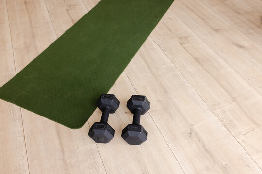 Pair of black hexagonal dumbbells are resting on light hardwood floor near green yoga mat