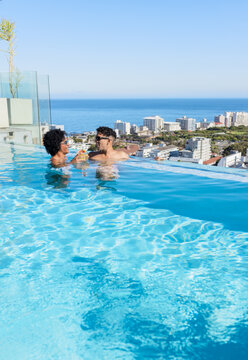 African American couple in swimwear standing in rooftop infinity pool holding drinks, copy space
