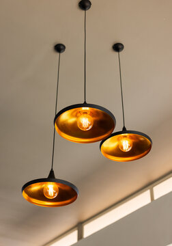 Three pendant lamps are hanging from beige ceiling, glowing filament bulbs and gold interiors