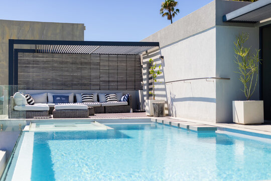 Rectangular swimming pool is reflecting turquoise water under pergola shadows on concrete deck