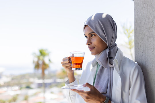 African American woman wearing headscarf, leaning on balcony, holding cup and saucer, copy space