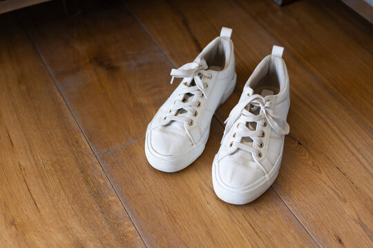 White canvas sneakers sitting side-by-side on warm hardwood floor, showing scuffed toe caps