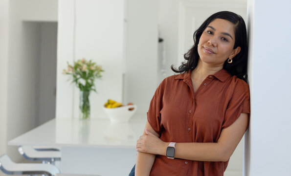 Midadult woman wearing rust blouse leaning against wall at island with smartwatch, copy space