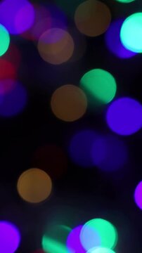 Una toma de cerca de varias luces de colores en forma de c&iacute;rculos en movimiento en la oscuridad. Desenfoque. Video vertical