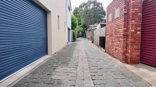 Narrow cobblestone laneway with garage doors and rear property access in an Australian inner-city neighbourhood. Urban service access behind residential houses in Melbourne.