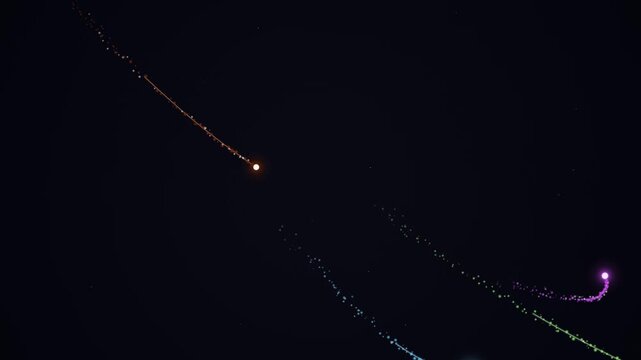Aerial view of colorful kites flying in the dark night sky with vibrant trails of light.