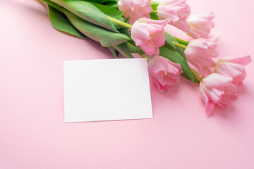 Pink tulips bouquet with blank card on pastel background. Spring floral greeting card, top view, copy space © Viktoriya