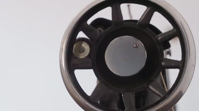 Close up black sewing machine wheel in house studio, homemaker mending patch, iron rim and central dial, textured metal detail, soft neutral lighting, minimalist domestic atmosphere