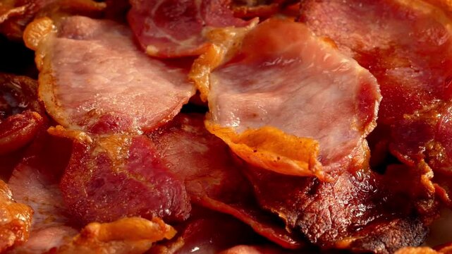 Pieces of crispy flavorful bacon fried in frying pan, macro closeup shot. Video of cooking sliced organic bacon. Splashes of fat scatter in the pan.