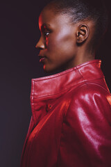 Profile portrait of confident black woman with dark skin wearing red leather jacket against dark background. Concept for fashion, style, and beauty with dramatic lighting and modern look. © SHOTPRIME STUDIO