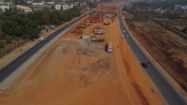High angle view of roadside construction with trucks and excavators standing in the dirt next to a busy highway in Abuja, FCT, Nigeria