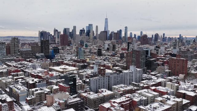 Snow flurries flying across Manhattan skyline in winter, revealing dense high-rise architecture, cold gray sky and urban atmosphere over New York City. Aerial wide shot. One World Trade Center in back
