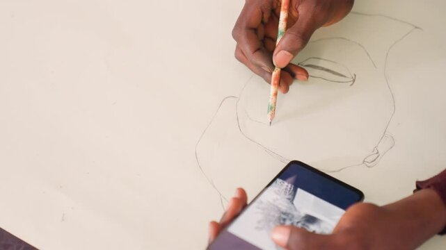 Black man sketching portrait from phone reference. Closeup hands drawing pencil outline on large paper, dotted construction lines, grayscale reference visible on phone screen, quiet studio atmosphere,