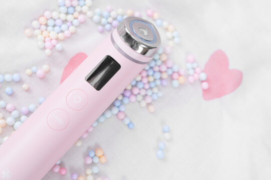 Bar, Montenegro: February 6, 2026: Pink handheld medicube booster pro skincare device with metal treatment head placed on white fabric among pastel beads pink heart shapes, minimal spa flat lay