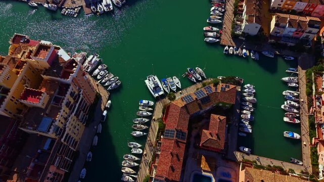 Boats are lined up in a canal near several buildings. The area is filled with water and greenery. The scene takes place during the day with clear visibility.