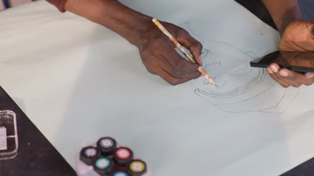 Black artist sketching portrait on paper using gouache palette and pencil, creating dotted guide lines while referencing phone for pose. Closeup hands show deliberate strokes, textured paper, patient