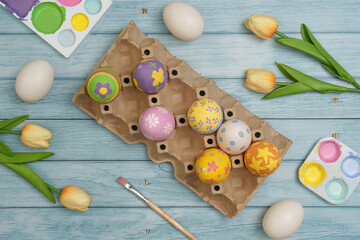 Fototapeta premium Easter Crafting. Decorated eggs in an egg carton with tulips on a wooden background.