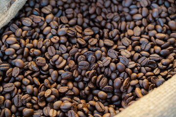 Obraz premium Roasted Coffee Beans: A close-up view of roasted coffee beans in a burlap sack, the rich texture and deep brown tones evoking the aroma of freshly brewed coffee.