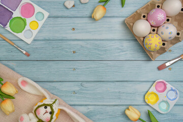 Fototapeta premium Easter Fun. Colorful eggs and a bunny toy on a wooden table with paint supplies.