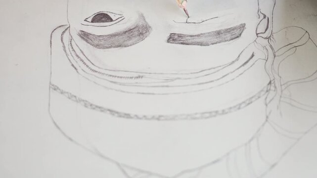 Closeup black sketch of mask, intricate stippling and shading around eye forms, pencil tip creating textured dots on white paper, studio table vantage with subtle shadow, precision technique