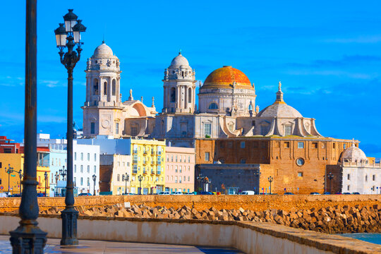 Stunning Cadiz Cathedral in Cadiz, Spain, glowing under a bright blue sky beside the ocean. Its golden dome and historic architecture create breathtaking coastal view