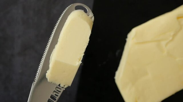 Close up video of a butter knife holding a slice of butter over a dark background with more butter visible