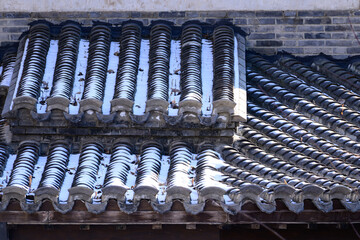 Sunlight illuminates the remaining snow on the traditional grey tiles of a Qing dynasty folk house roof, highlighting the textures of both the weathered tiles and the melting snow.