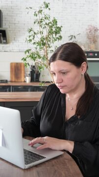 Woman typing on laptop at kitchen table while working from home. Freelance accounting and financial record-keeping concept.
