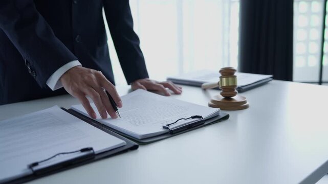 Lawyer holding pen checking documents with gavels on desk