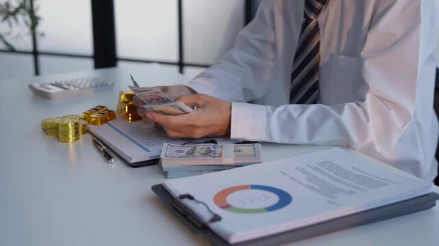 Businessman counting cash with gold bar and stacking coins on table