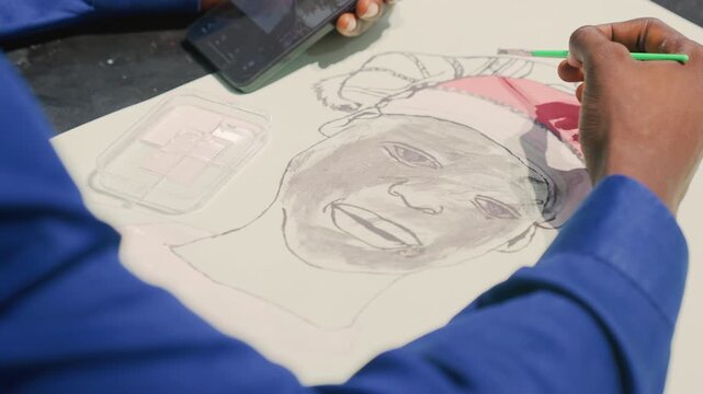 Black artist painting colorful portrait with brush, overhead view of bluesleeved hand adding red wash and fine detail, smartphone reference on table, layered tones and focused studio workflow,