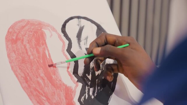 Wide shot artist painting black heart on canvas, visible hand and green brush sketching red fill and dark outline, calm indoor studio with vertical blinds, focused pacing, instructional vibe